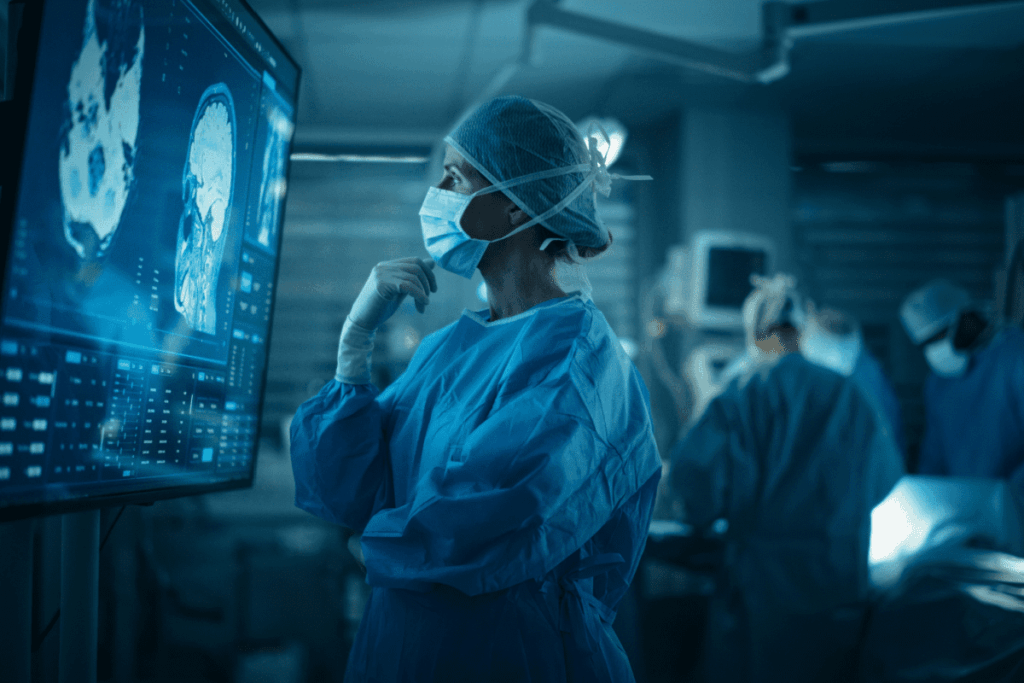 A surgeon reviews medical images on a screen as other surgeons perform surgery behind her. 